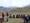 a group of outdoor enthusiasts sitting in a circle in an alpine meadow, listening to two instructors