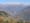 a hillside village in a forested valley, with snow-capped peaks in the backdrop